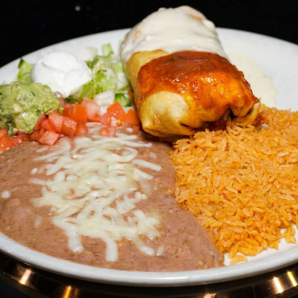 Mexican plate featuring a cheese-covered burrito, refried beans, Mexican rice, guacamole, pico de gallo, lettuce, and sour cream.